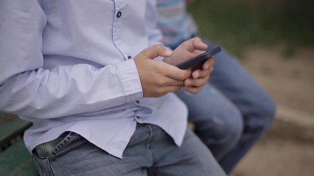 Close up of Young boy sitting on the bench and play online games during school break