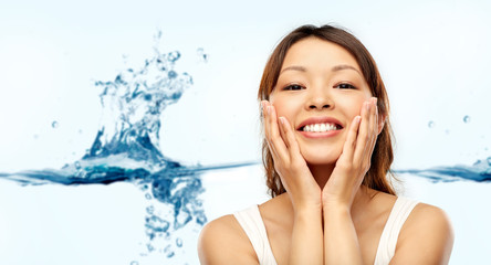 beauty, skin care and hydration concept - happy smiling young asian woman touching her face over...