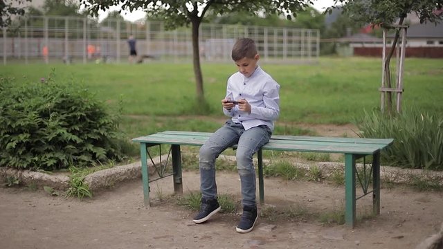 Handome young boy sitting on the bench and play online games during school break