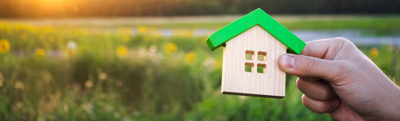 Wooden house in the hands in the sunset background. Real estate concept. Eco friendly home. Symbol...