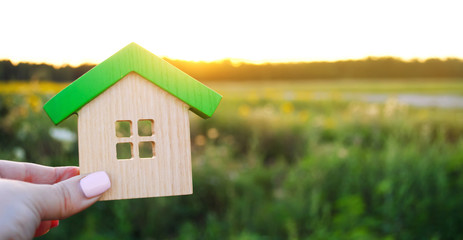 Wooden house in the hands in the sunset background. Real estate concept. Eco friendly home. Symbol of happy family life. Buy a housing outside the city. Search for hotel on vacation. Selective focus