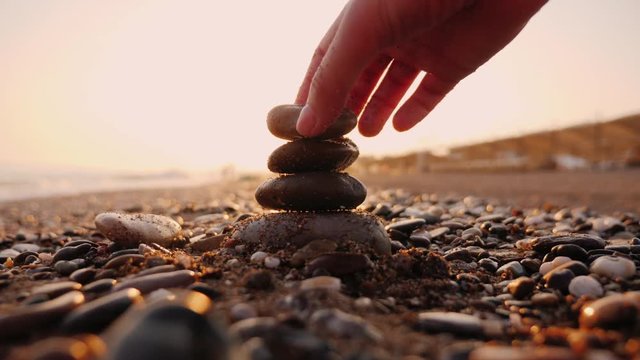 Hand puts stones in the pyramid, the sun's rays shine through his fingers