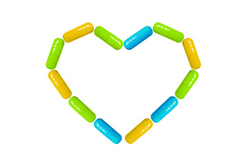Heart shape made from blue, green and orange pills and capsules isolated on white background with copy space. Vitamins concept