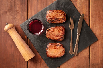 Sirloin or fillet beef steaks and red wine, top shot on a black slate plate, with a pepper mill
