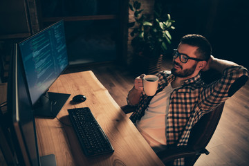 Close up photo handsome enjoy mug hot beverage he him his guy relaxing big chair coder php css development outsource IT processing two monitors table office agency wear specs formalwear shirt