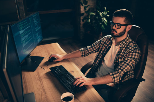 Close up photo not smiling handsome he him his guy coder typing php css keyboard development outsource IT processing language two monitors table office agency wear specs formalwear plaid shirt