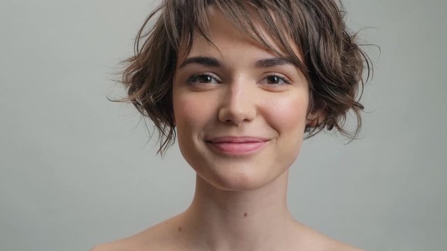 Beautiful young woman with natural skin smiling while looking at the camera over grey background isolated