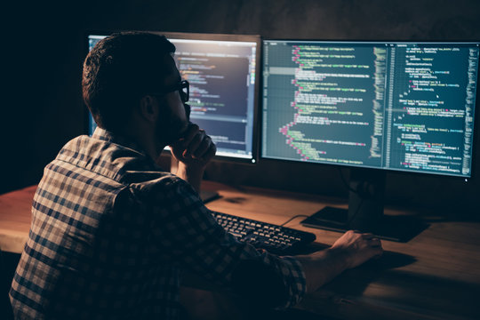 Close up back rear behind photo stubble handsome he him his guy pensive hands arms chin coder code development outsource IT processing two monitors table office wear specs formalwear plaid shirt