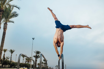 fitness, sport, training, calisthenics and lifestyle concept - young man doing witch handstand on the calisthenics bars