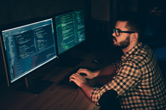 Close up side profile photo handsome he him his guy coder typing php css html keyboard development outsource IT processing language two monitors table office agency wear specs formalwear plaid shirt