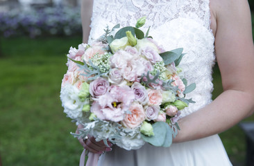 beautiful wedding bouquet of different colors in the hands of the bride on a white lace wedding dress. In the park on the street. Wedding concept.