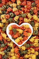 Fototapeta premium Trottole tricolour pasta in a heart shaped dish and loose forming an abstract background.