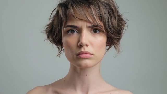 Serious young lady with natural skin becoming scared while looking at the camera over grey background isolated