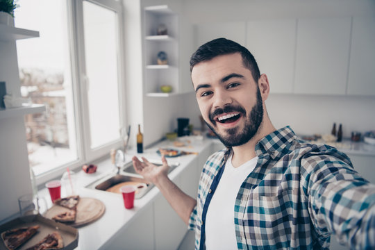 Self-portrait of his he nice attractive cheerful cheery glad bearded guy wearing checked shirt having fun inviting you visit modern light white interior style kitchen indoors