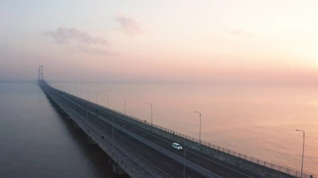 Beautiful aerial view of Suramadu bridge at sunrise time on Madura strait from Surabaya city to Madura island, East Java, Indonesia. Shot in 4k resolution from a drone flying from left to right
