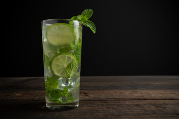 Mojito drink with lime, lemon and mint on wooden table.