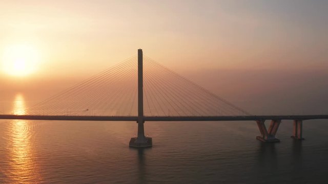 Exotic aerial view of silhouette of Suramadu bridge and sunlight reflection on Madura strait at sunrise in Surabaya, East Java, Indonesia. Shot in 4k resolution from a drone flying from right to left