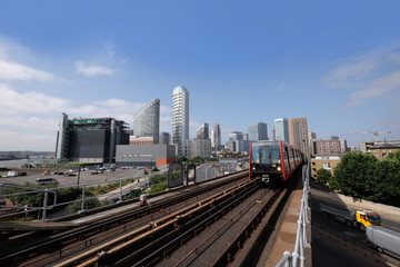 Fototapeta na wymiar London, United Kingdom 6th July 2019: Canary Wharf skyline seen from Tower Hamlets, DLR Docklands Light Railway train in foreground on summer day, logos removed