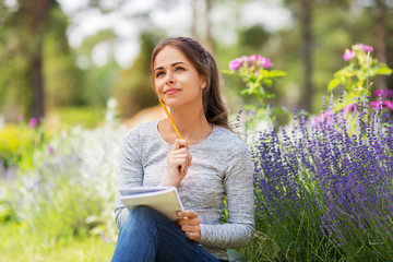 gardening and people concept - young woman writing to notebook at summer garden