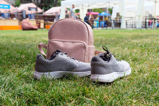 Pink leather female backpack and gray sneakers on a green lawn in the park. The concept of outdoor recreation, hiking in the summer season.