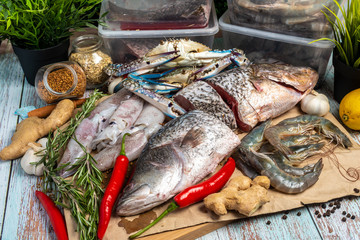 Fresh Seafood - Golden Snapper, Sea Bass, Prawns, Crabs, and Squids - on a wooden table surrounded by raw ingredients.