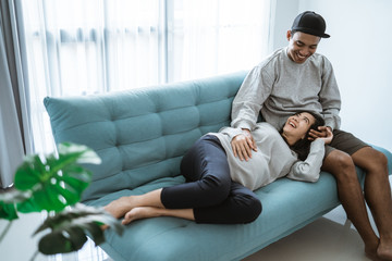 a pregnant woman lay on her husband's lap while sitting relaxed on the living room sofa