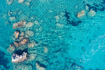 Aerial view of turquoise sea water and rocks by the seashore.