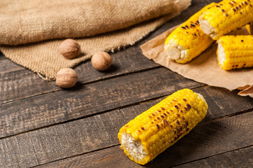 Heap of fried corn cobs near whole greek nuts lies on crumpled paper and old brown rustic wooden table. Copy space
