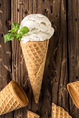Top view white ice cream in waffle cone on rustic background
