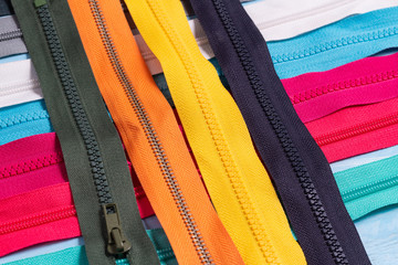 Pack a lot of colorful plastic zippers stripes with sliders pattern for handmade sewing tailoring on the blue denim background close up selective focus