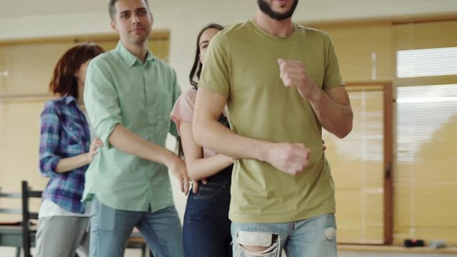 Group of four young friends enjoying dancing Latin lambada dance holding each other on waist and walking around room at home party