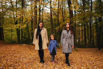 Fototapeta premium Mom and two daughter have fun in ther park. Youngest daughter collect leaves and smile. Happy family walking in the forest