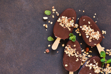 Chocolate popsicle with granola and nuts. Ice cream on a concrete background. Top view.