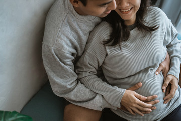 happiness husband and wife feel pregnancy, sit back together on the couch while holding the belly of a pregnant wife