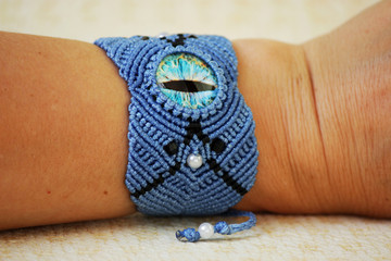 blue bracelete with white beads and the dragon's eye on the hand from waxed thread in the technique of macrame. Handmade. put on hand