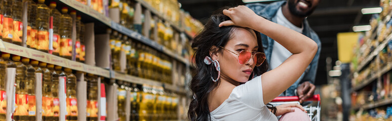 panoramic shot of african american man near stylish asian girl in sunglasses in store