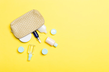 Top view of female cosmetics bag with dropped out cosmetic products on yellow background. Bodycare concept with copy space