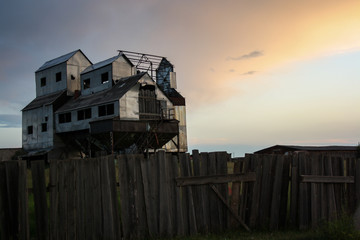 The old abandoned granary in the rays of sunset, like a moving castle. Wooden fence in the foreground