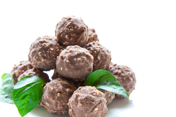 round chocolate candy with nuts in the form of a pyramid with green leaves on a white background isolate