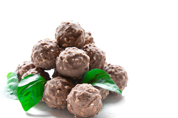 round chocolate candy with nuts in the form of a pyramid with green leaves on a white background isolate