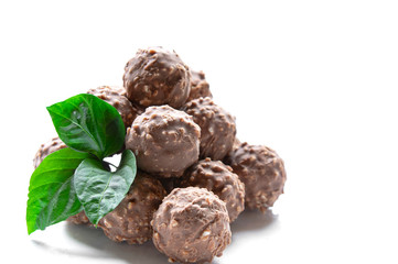 round chocolate candy with nuts in the form of a pyramid with green leaves on a white background isolate