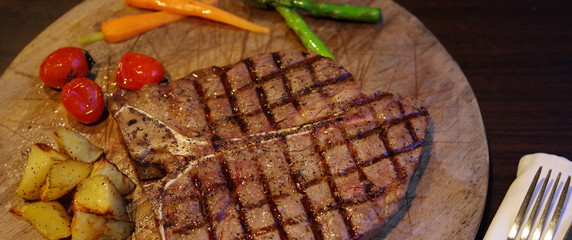 Grilled T bone steak with potato, carrot, cherry tomato and asparagus on wood plate
