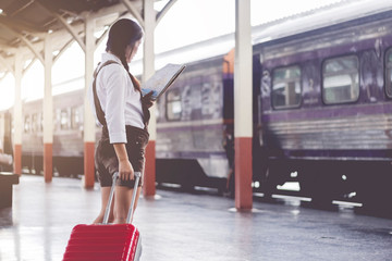 Asian woman pregnant travel look at the map with red suitcase at railway station travel,Holiday travel concept.