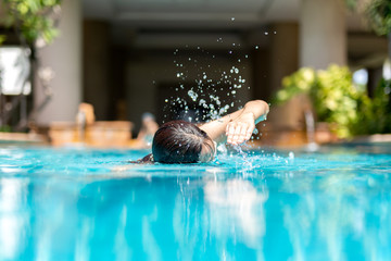 Unidentified woman doing front crawl swimming in swimming pool on vacation.
