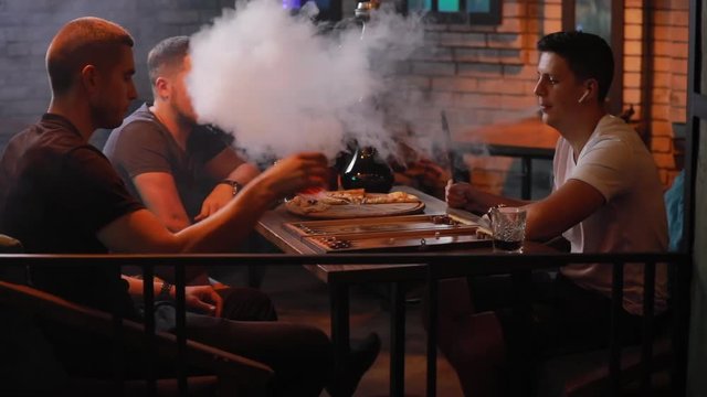 Men friends smoking hookah playing backgammon in a bar