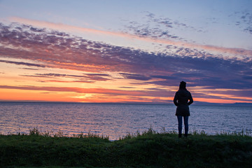 Fototapeta na wymiar Travel vacation and tourism concept,Summer time Backpacker Standing to watch the midnight sun and rest Ocean view at the Iceland.