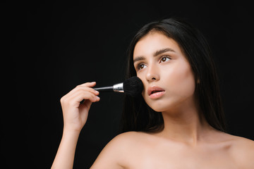Obraz premium Beauty woman applying makeup. Beautiful young woman applying cosmetic paint brush. Brunette girl apply make-up. Beauty Face. Isolated on black background.