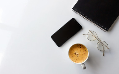 business concept. top view of office desk workspace with smartphone, nostbook, glasses and hot coffee cup on white table background. over light