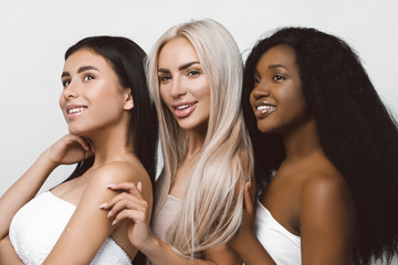 Beauty photo of three smiling multiracial women with different types of skin: Caucasian, African american and Asian girls, isolated over white background. Beautiful  young women with natural make-up.