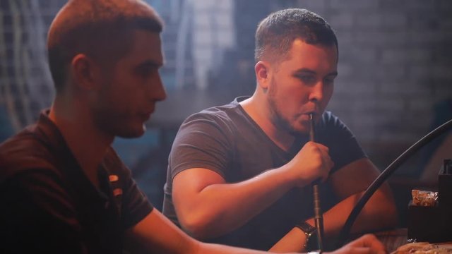 Men friends smoking hookah playing backgammon in a bar